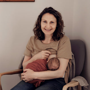  A young smiling woman, sitting in a comfortable chair breastfeeding her newborn baby