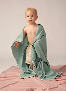  Toddler with green wrap over shoulders stands on pink blanket